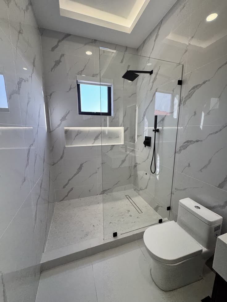 Marble-tiled walk-in shower with frameless glass and matte black fittings