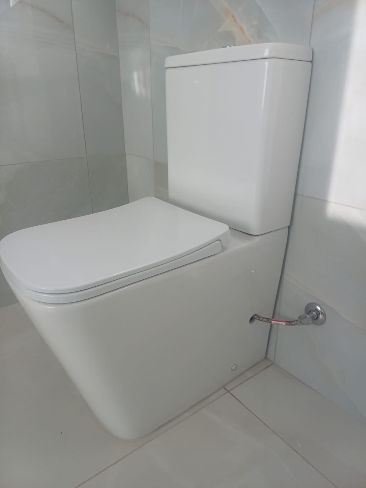 Newly installed back-to-wall toilet in a marble-tiled bathroom