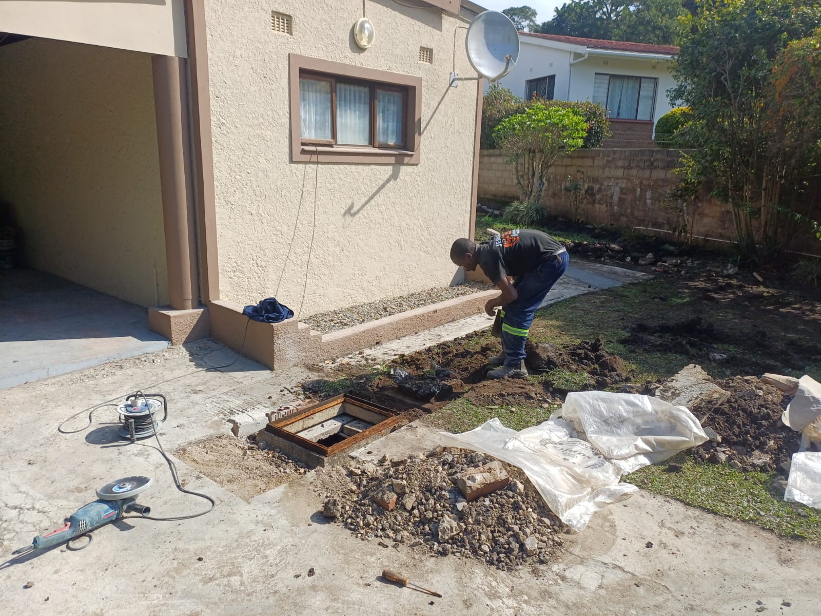 Plumber excavating a driveway to reach an underground drain inspection chamber
